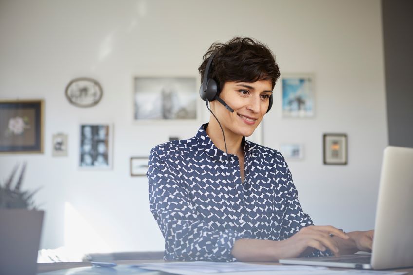 An individual sits in front of a laptop, wearing a headset with a microphone