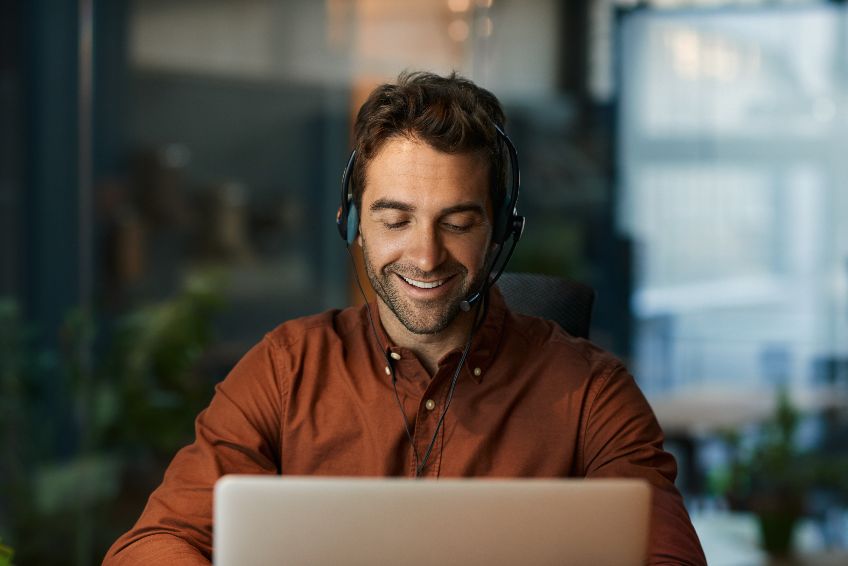 An individual sitting in front of a laptop, wearing headphones