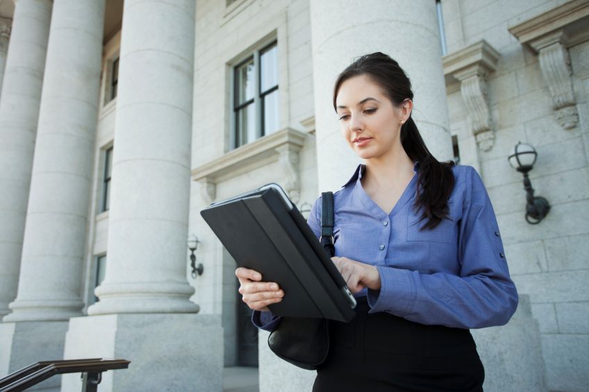 An individual standing in front of a building with large columns, holding a tablet