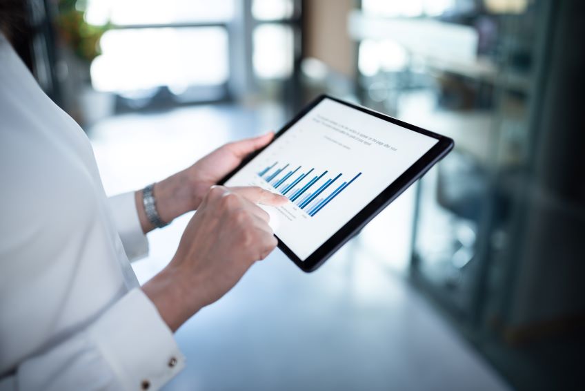 A person holding a tablet displaying a bar graph, with their hand pointing at one of the bars, in an indoor setting