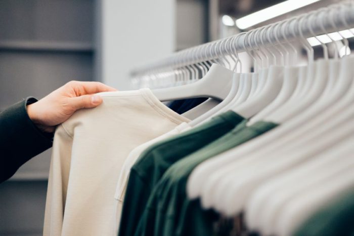 A close-up view of a person’s hand pulling out a light-colored shirt from a rack of clothes