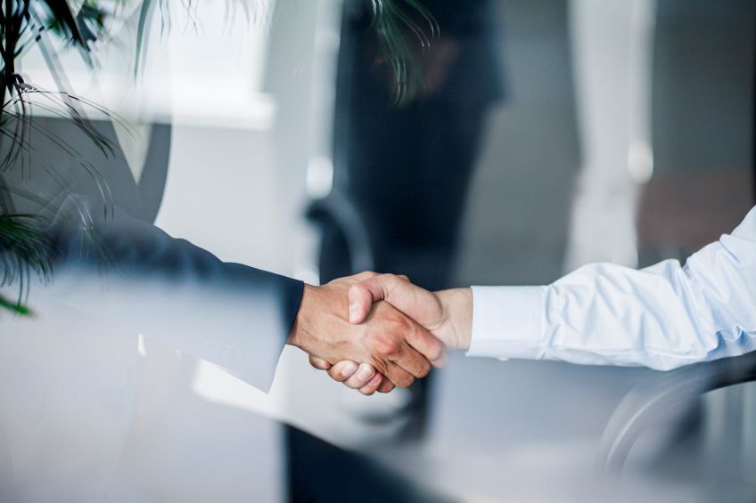 Two individuals engaged in a handshake through a glass surface