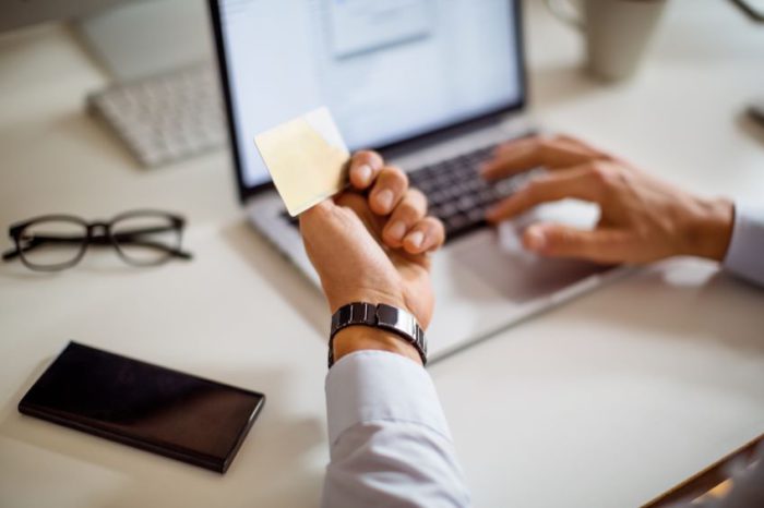 An individual types on a laptop with one hand while they hold a credit card in the other