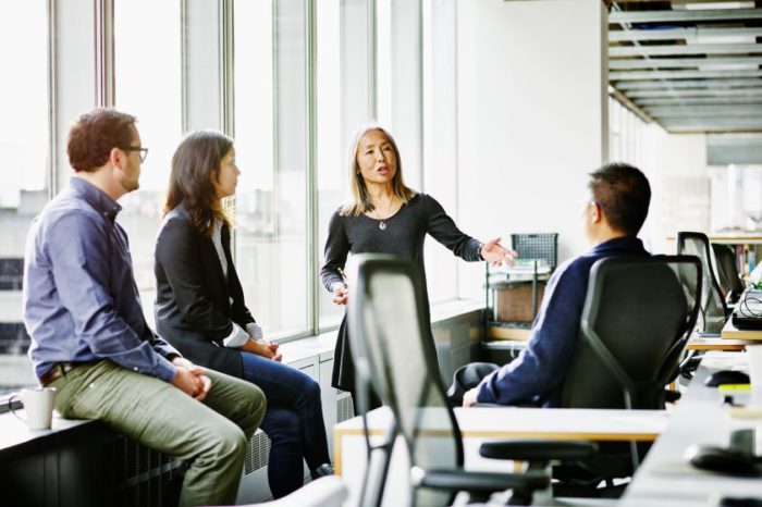 Four professionally dressed individuals gathered around in an office with large windows