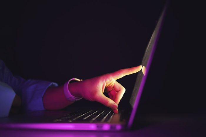 A side view of a laptop in a low-light environment while an individual's finger touches the screen