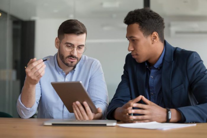 Two businesspeople sitting at a table look at information on a tablet