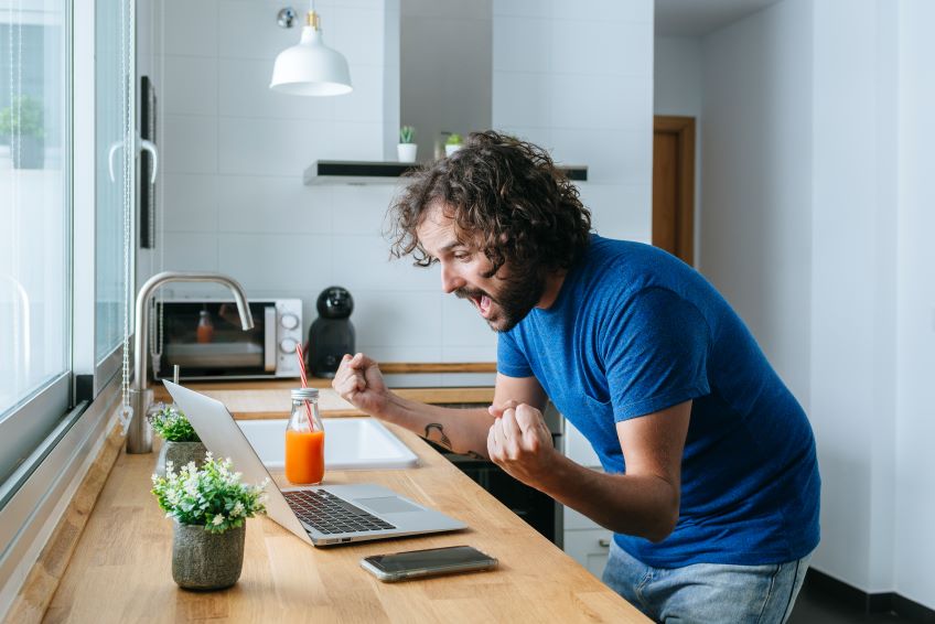 man is cheering for video on laptop