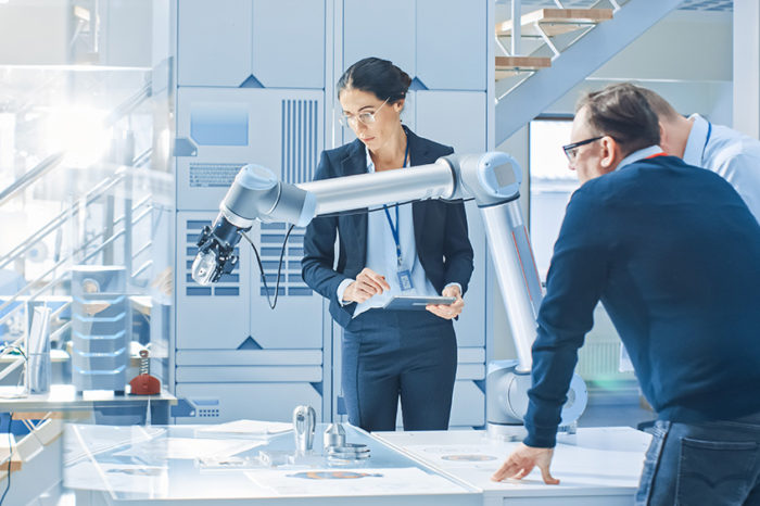 Three business people working alongside a robotic arm in a lab