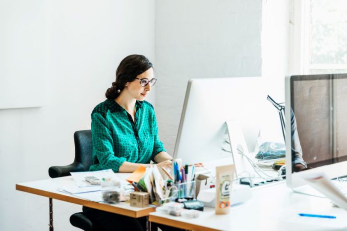 Woman in green working at a white desk on computer