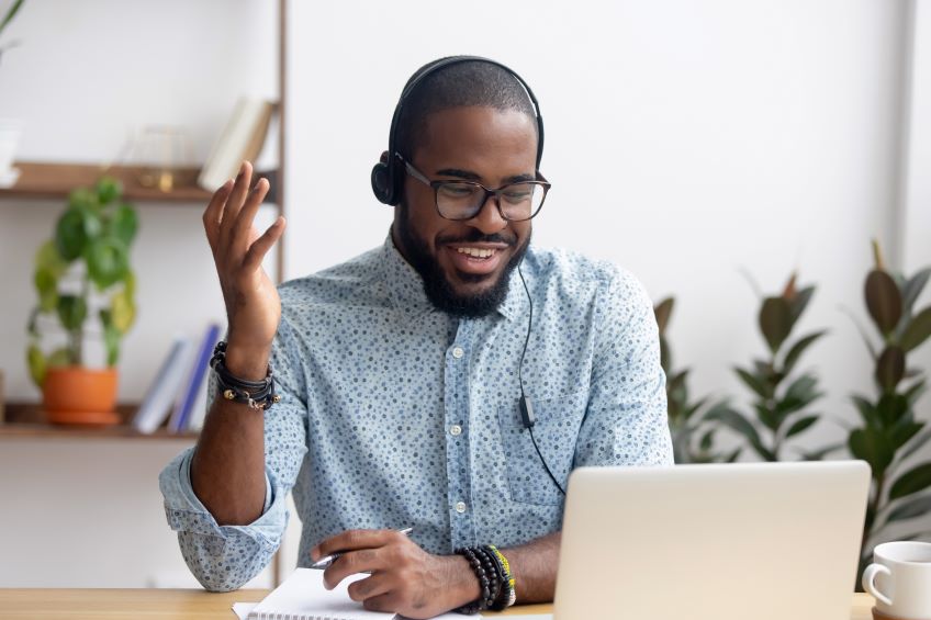 A participant in a Zoom call smiling and wearing headphones while looking at a tablet on a desk