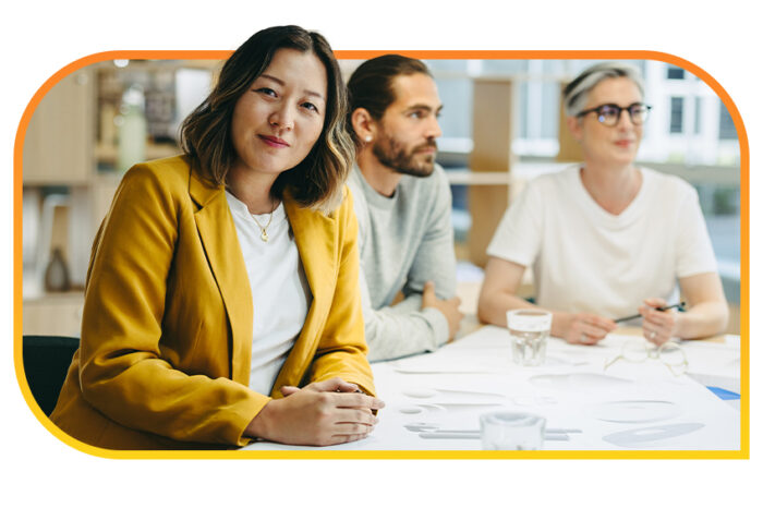 Person in a yellow jacket sitting next to two other people at a conference table.