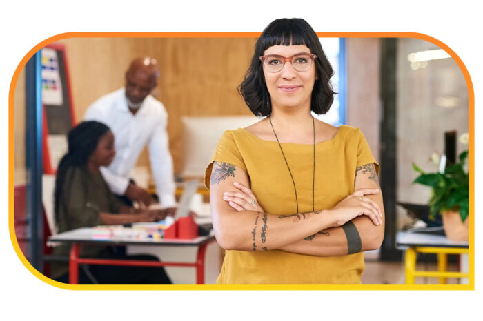 Person in yellow shirt standing in front of an office space and two people together at a desk.