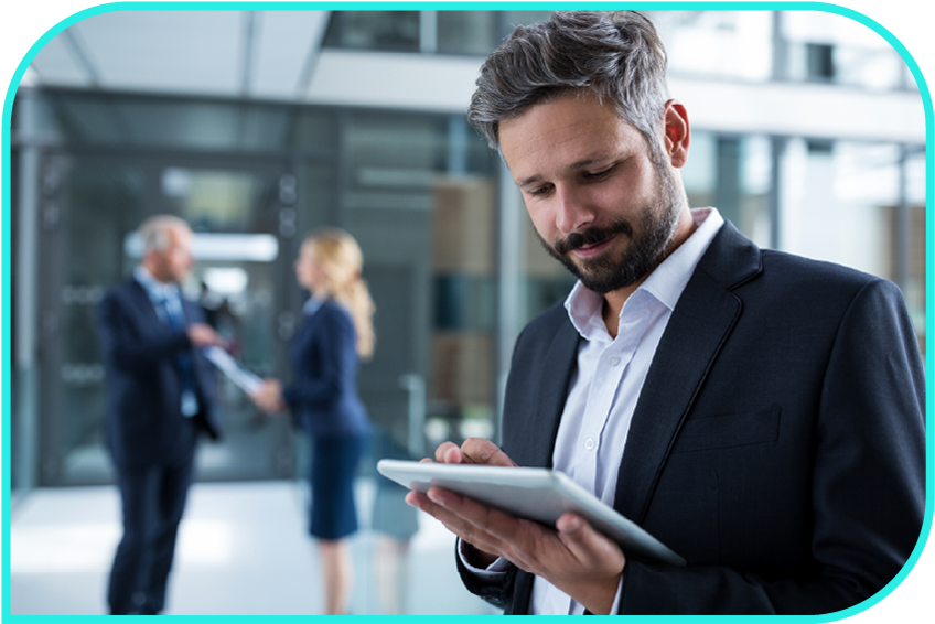 A man in business attire studies a tablet outside an office as two people converse in the background