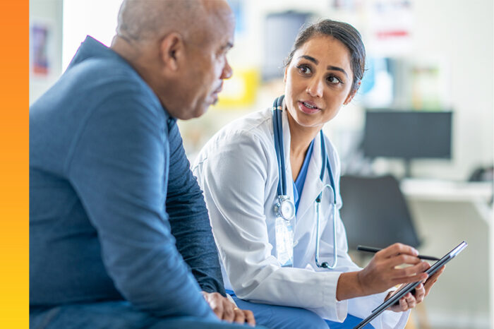 A healthcare professional in a white coat holding a clipboard is engaged in a discussion with a patient in blue in a clinical setting