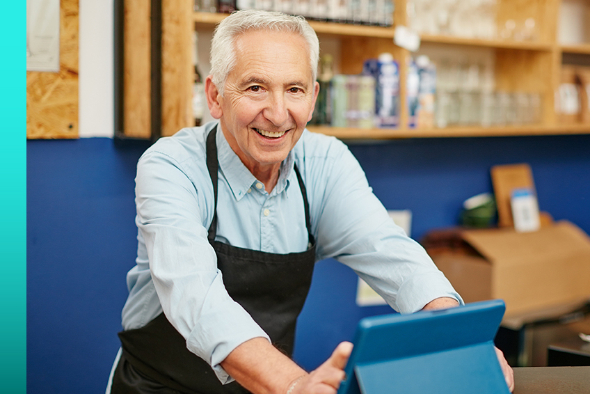 A person in an apron smiles while using a tablet device in a workshop