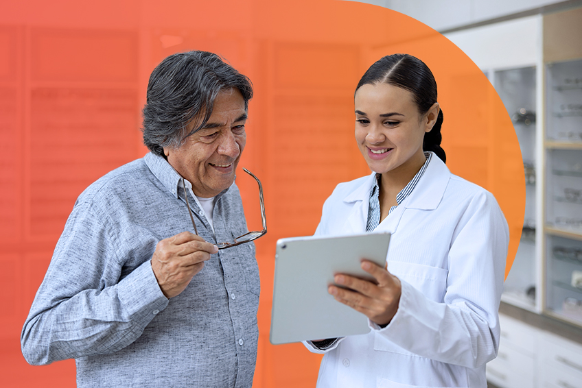 A healthcare professional in a lab coat talks with a patient in an office with glasses displayed in the background